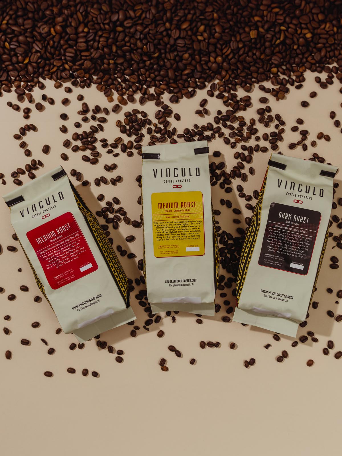 Three bags of coffee laying on a table with coffee beans scattered. 