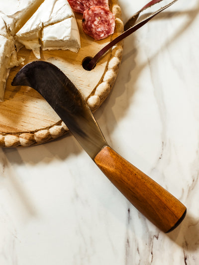 Horn cheese knife with wood handle on white marble counter with serving board.