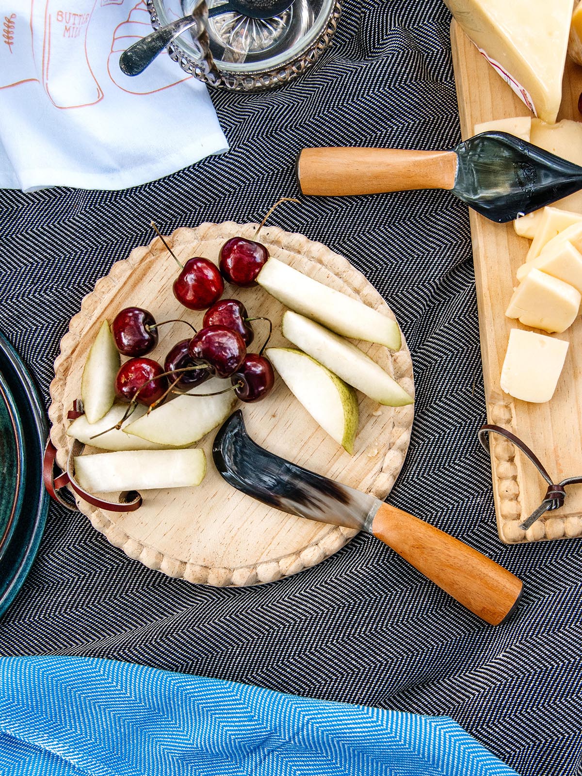 Artisanal spreader knife with a wooden handle, paired with fresh fruit and gourmet cheese on a rustic picnic setup, available at Joffa.