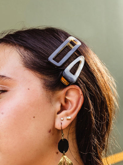 Close-up of a woman’s hair adorned with two geometric hair clips, paired with gold earrings featuring a black and gold drop design.