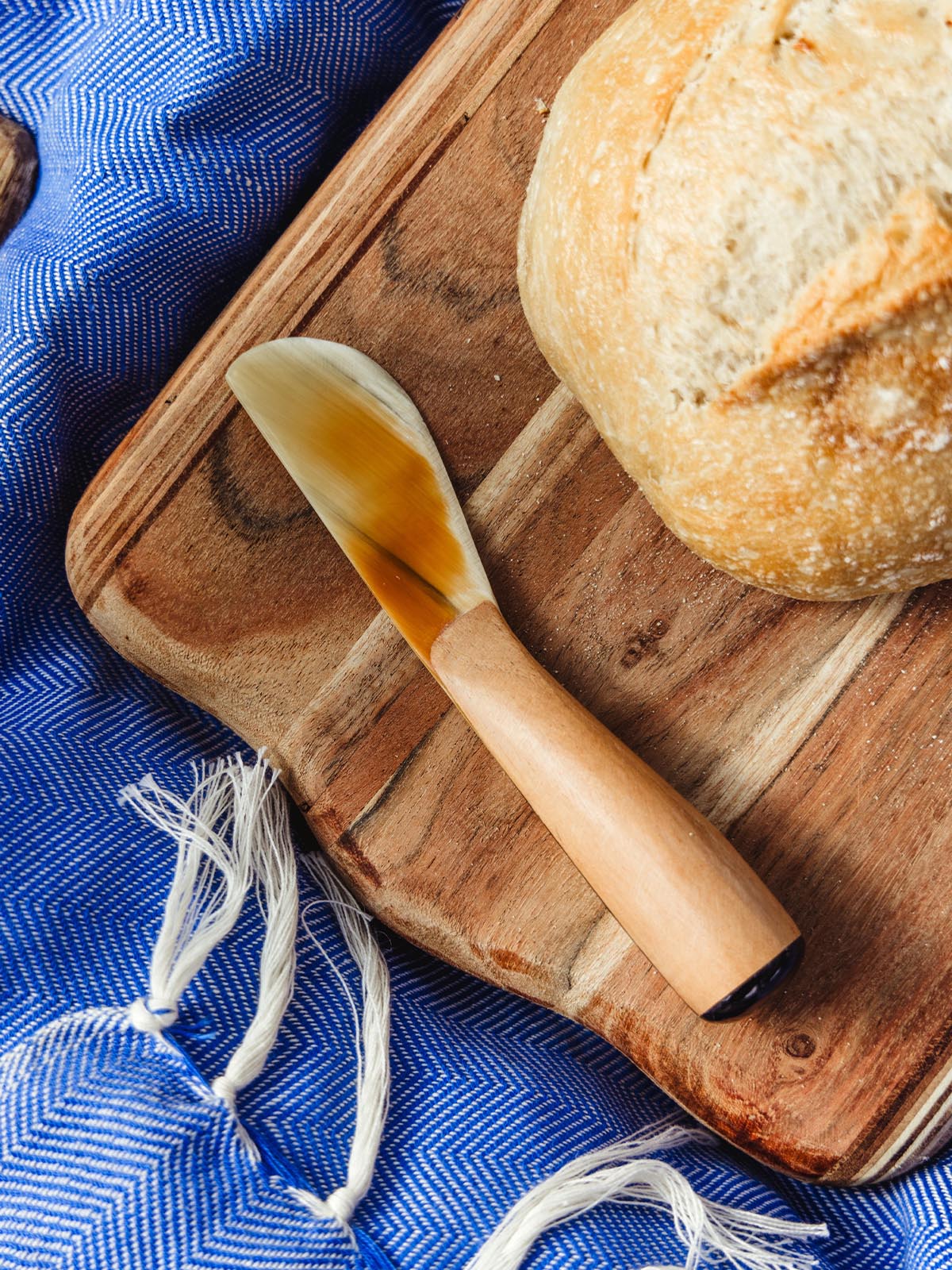 Artisanal butter spreader with a wooden handle on a wooden cutting board next to fresh bread, showcasing Joffa's handcrafted kitchen accessories.