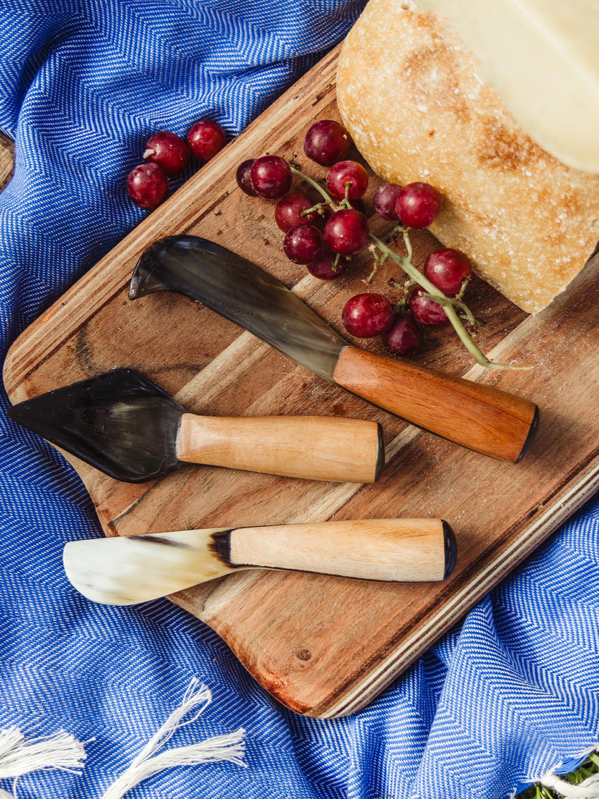 Set of artisanal kitchen knives with wooden handles, displayed on a wooden board with fresh bread and grapes, showcasing Joffa’s elegant kitchen tools.