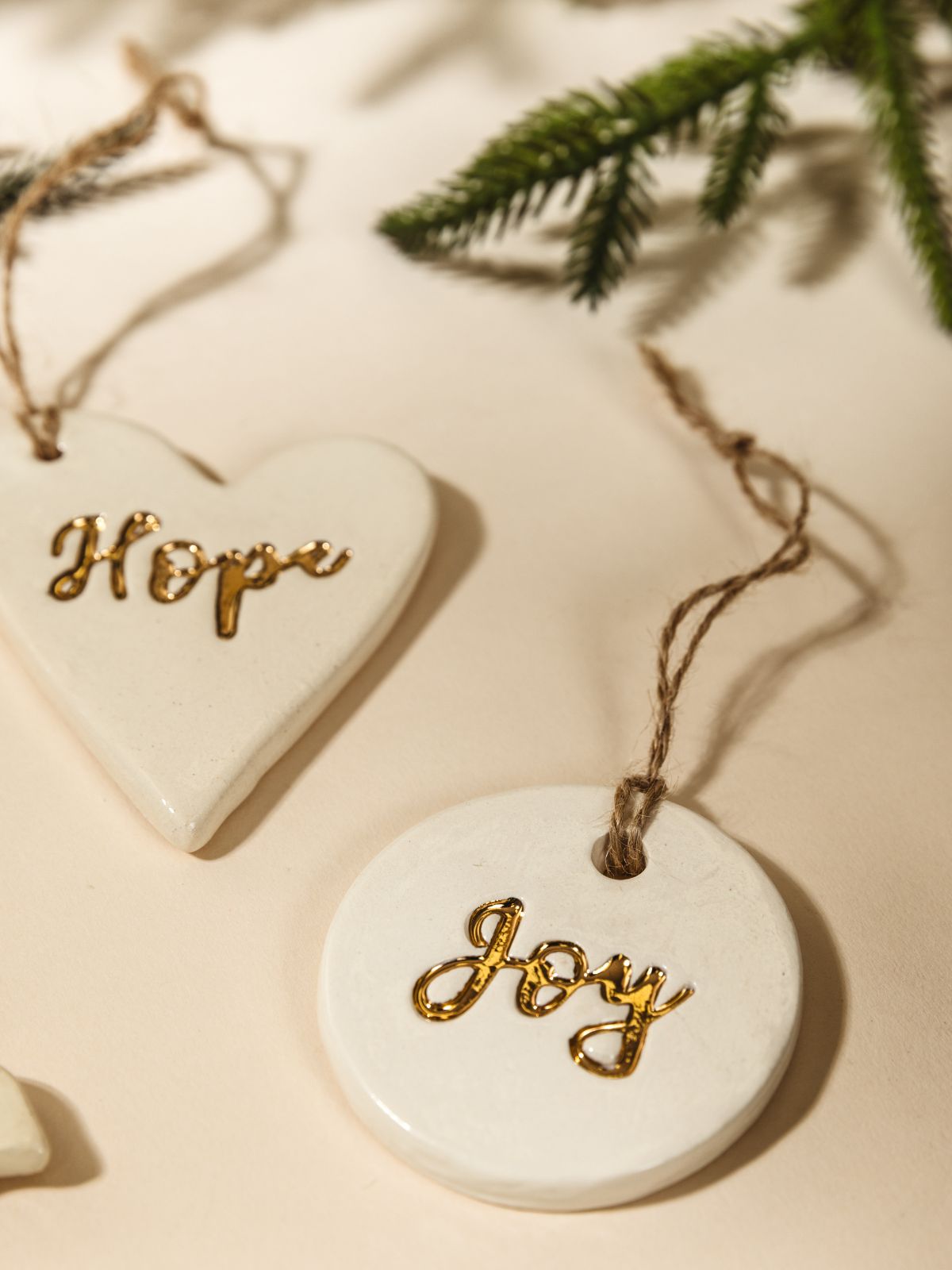 Close up of Gold Leaf Pottery Ornaments on cream background with Christmas greenery.