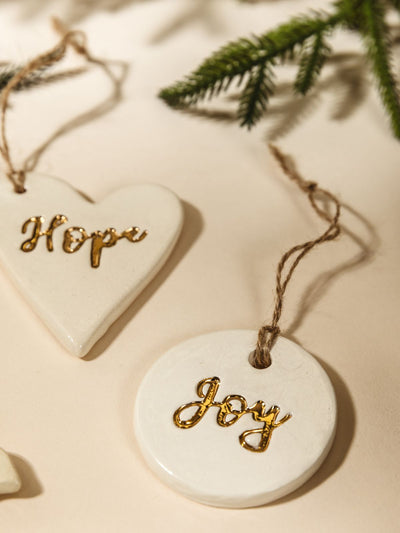 Close up of Gold Leaf Pottery Ornaments on cream background with Christmas greenery.