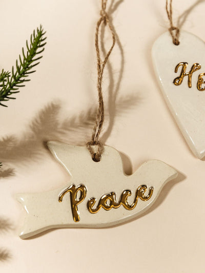 Close up of Gold Leaf Pottery Ornaments on cream background with Christmas greenery.