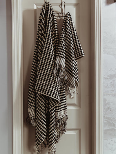 Two black and white patterned woven towels with fringe detail hanging on a door hook, offering a cozy and sophisticated home accent.