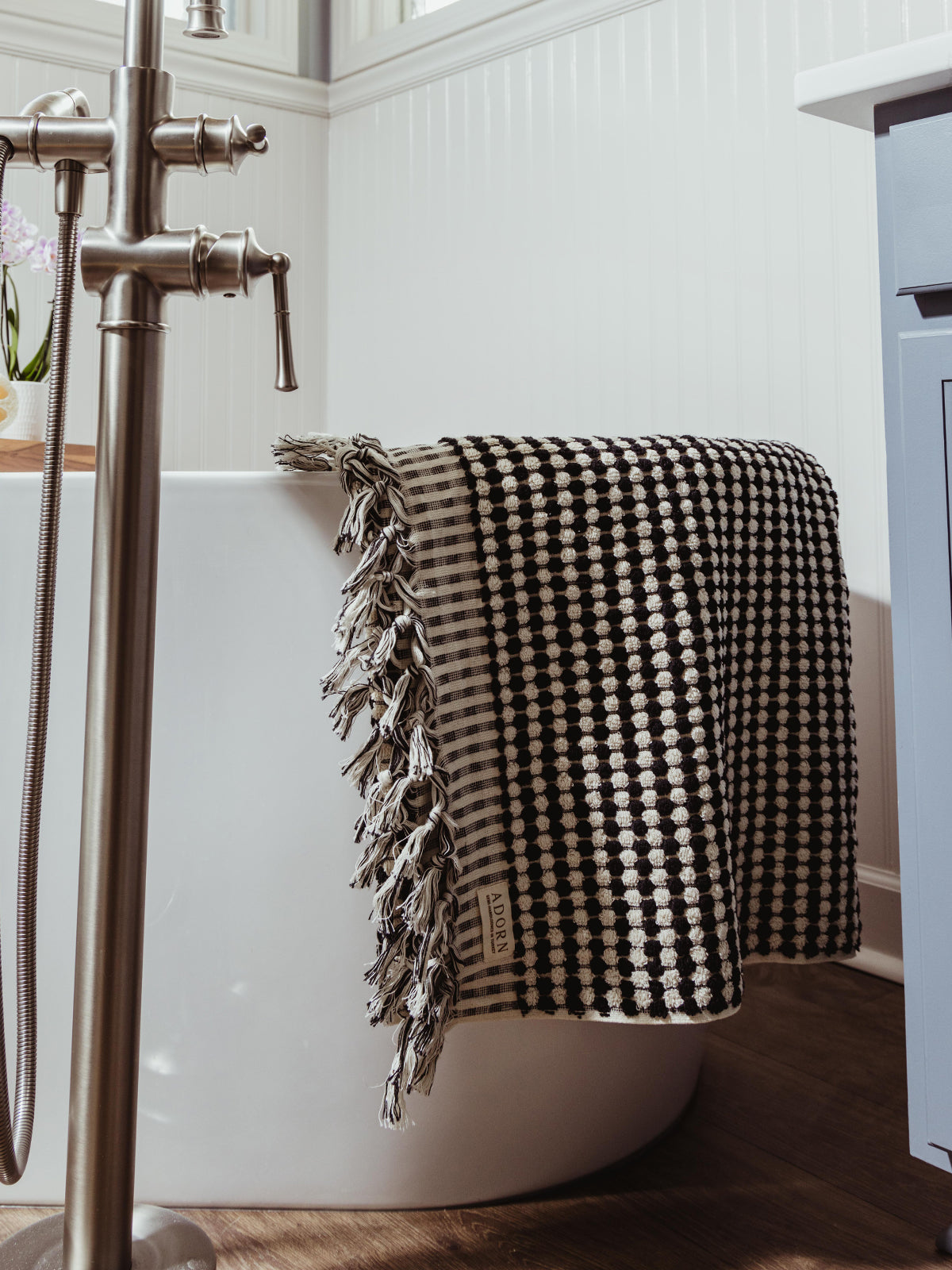 A black and white checkered woven towel with fringed edges draped over a modern freestanding bathtub, adding a stylish touch to the bathroom decor.