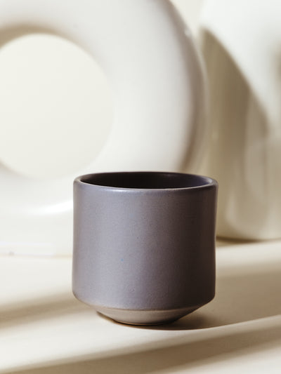 A single gray ceramic cup with a matte finish, showcased against a neutral backdrop with sculptural decor. Elegant and versatile drinkware for everyday use.