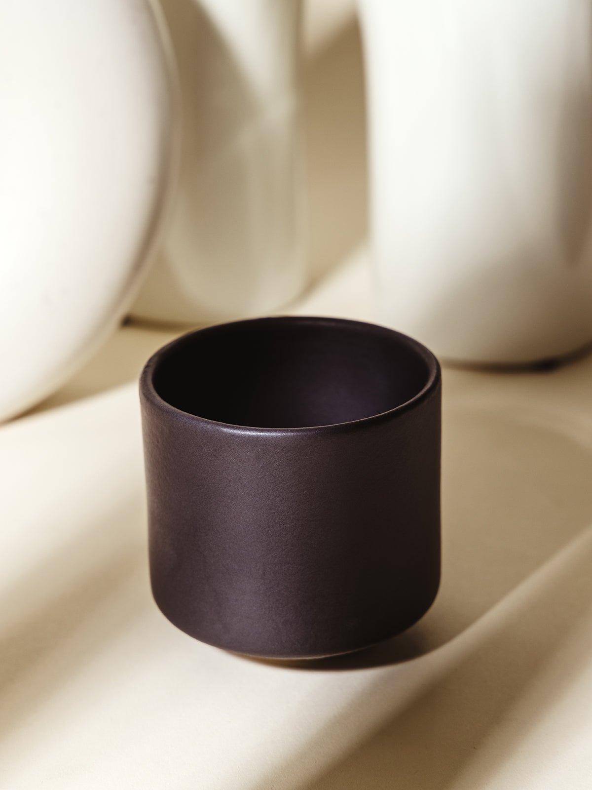 A sleek black ceramic cup with a matte texture, placed in a modern setting with sculptural elements. Perfect for minimalist kitchen aesthetics.