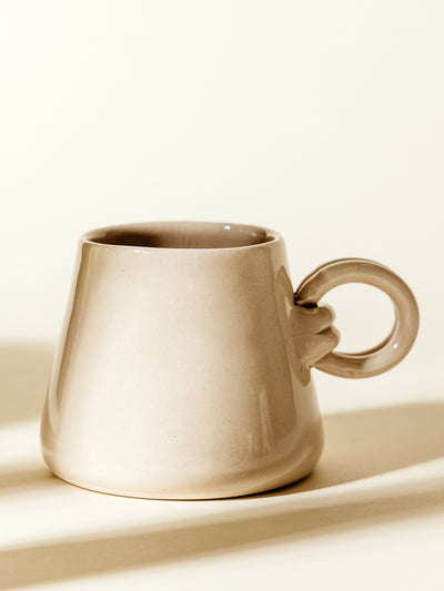 Minimalist beige ceramic mug with a smooth, glossy finish and a unique loop handle. Perfect for modern home decor and coffee lovers seeking stylish drinkware.