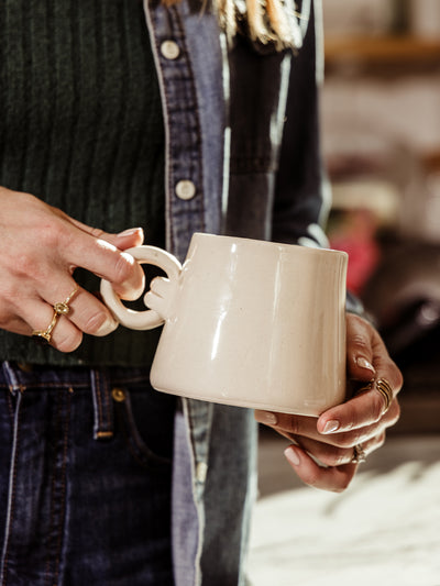 Close-up of a handcrafted ceramic coffee mug with a smooth finish and distinctive knotted handle, ideal for modern home aesthetics.