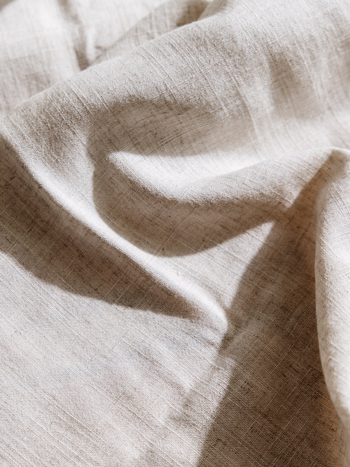 Detailed close-up of natural beige linen fabric, showing its breathable, textured weave, perfect for rustic table settings and soft, organic decor.