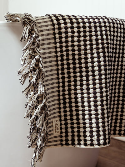 A close-up of a black and white checkered woven towel featuring the ADORN label, showcasing its intricate texture and handcrafted design.