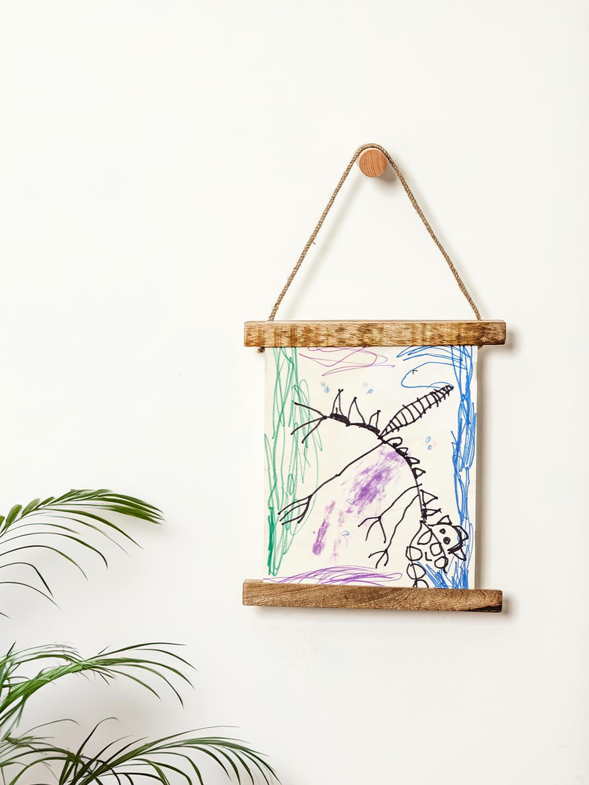 Children's drawing of a dinosaur displayed in a wooden art frame hanging on a wall.