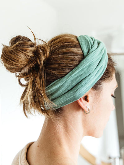 Woman wearing a mint green fabric wrap headband with her hair styled in a messy bun, showcasing the headband’s soft texture and comfortable fit.