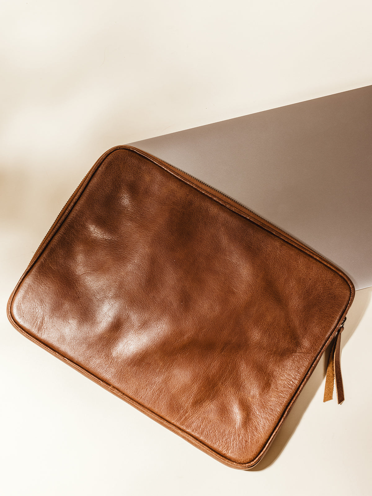 Laptop in brown laptop sleeve on cream background.