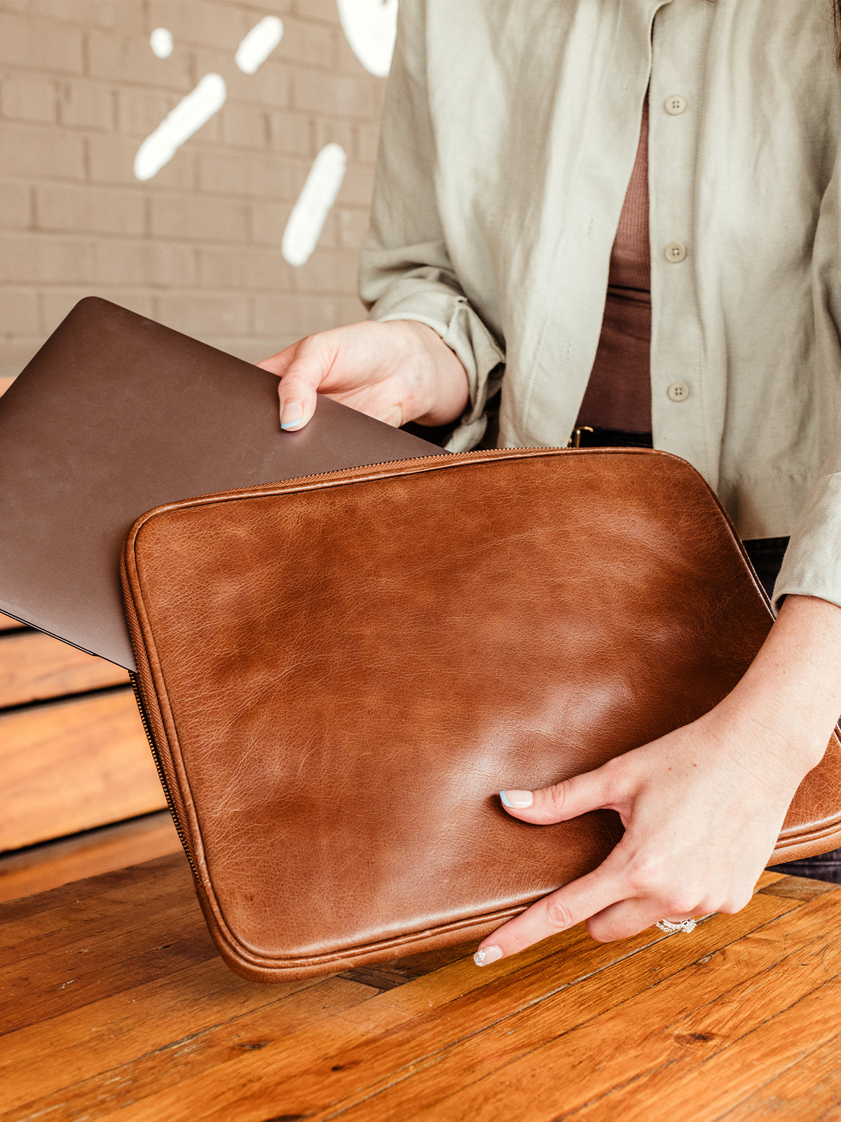 Female model putting laptop in brown leather laptop sleeve.