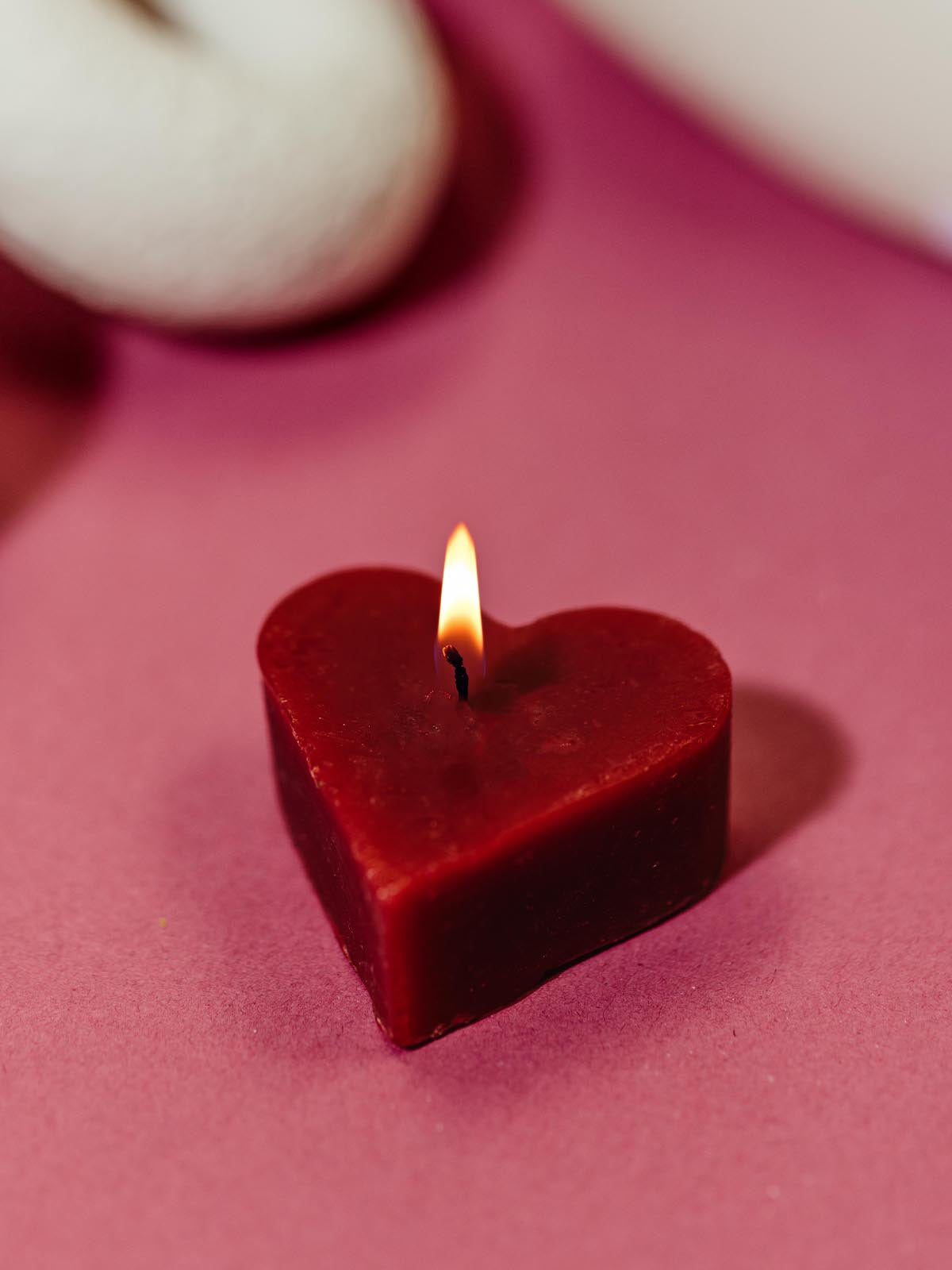 Single red heart-shaped beeswax candle burning on a red surface, adding a warm and romantic ambiance