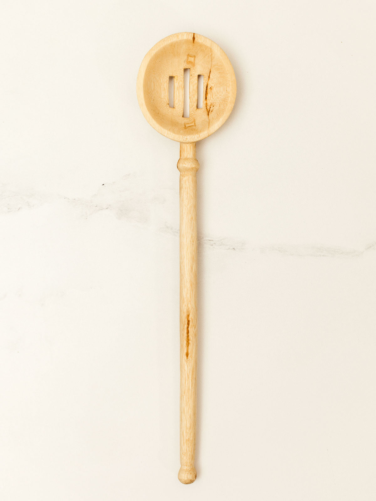 Wooden slotted spoon on white granite counter top.
