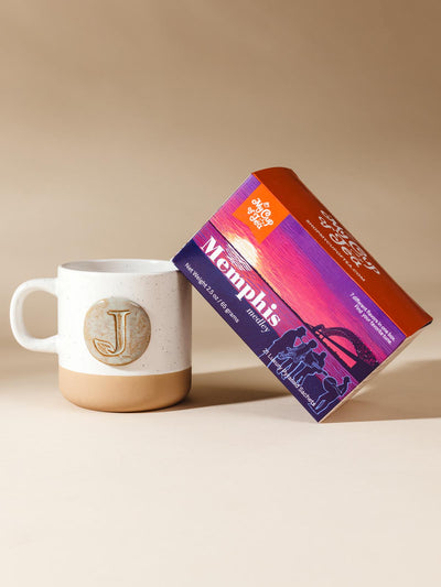 Box of memphis medley tea and mug on cream Background