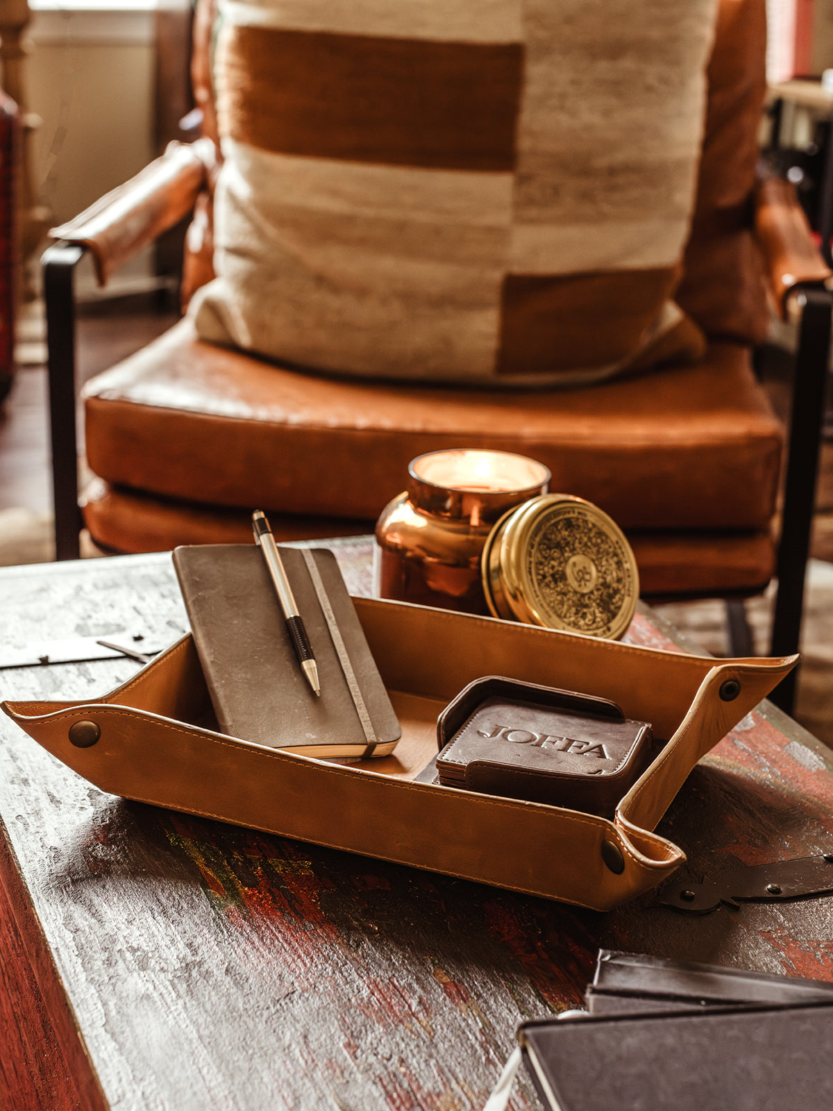 Large leather valet ray with note book and coasters placed inside. Valet tray is on a wood table in a living room setting.