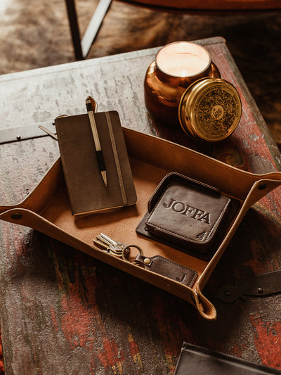 Large leather valet ray with note book and coasters placed inside. Valet tray is on a wood table in a living room setting.