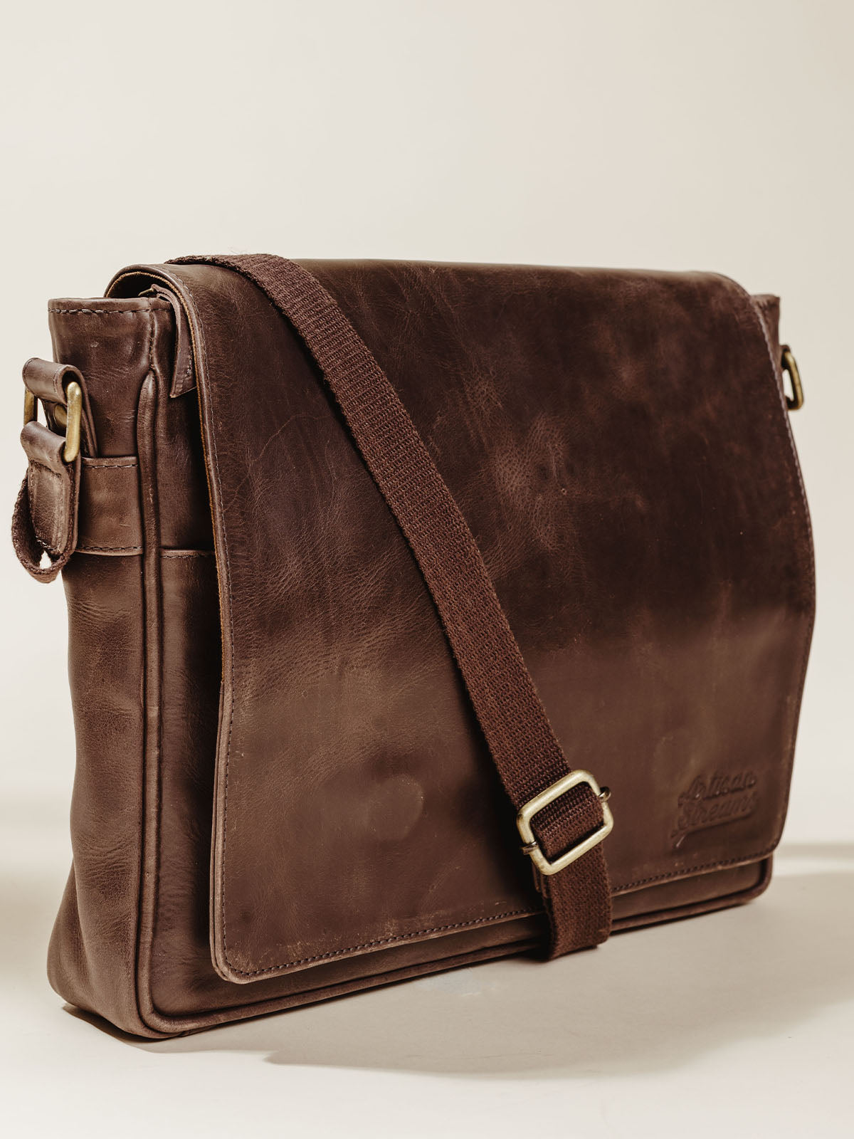 Dark brown Leather Farmaan Satchel with shoulder strap on cream background. 