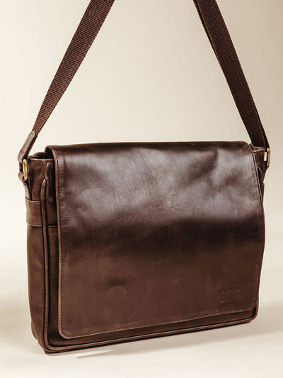 Dark brown Leather Farmaan Satchel with shoulder strap on cream background. 