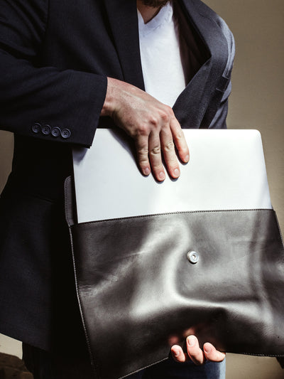 White male wearing a business blazer and jeans placing laptop in black envelope style laptop sleeve.