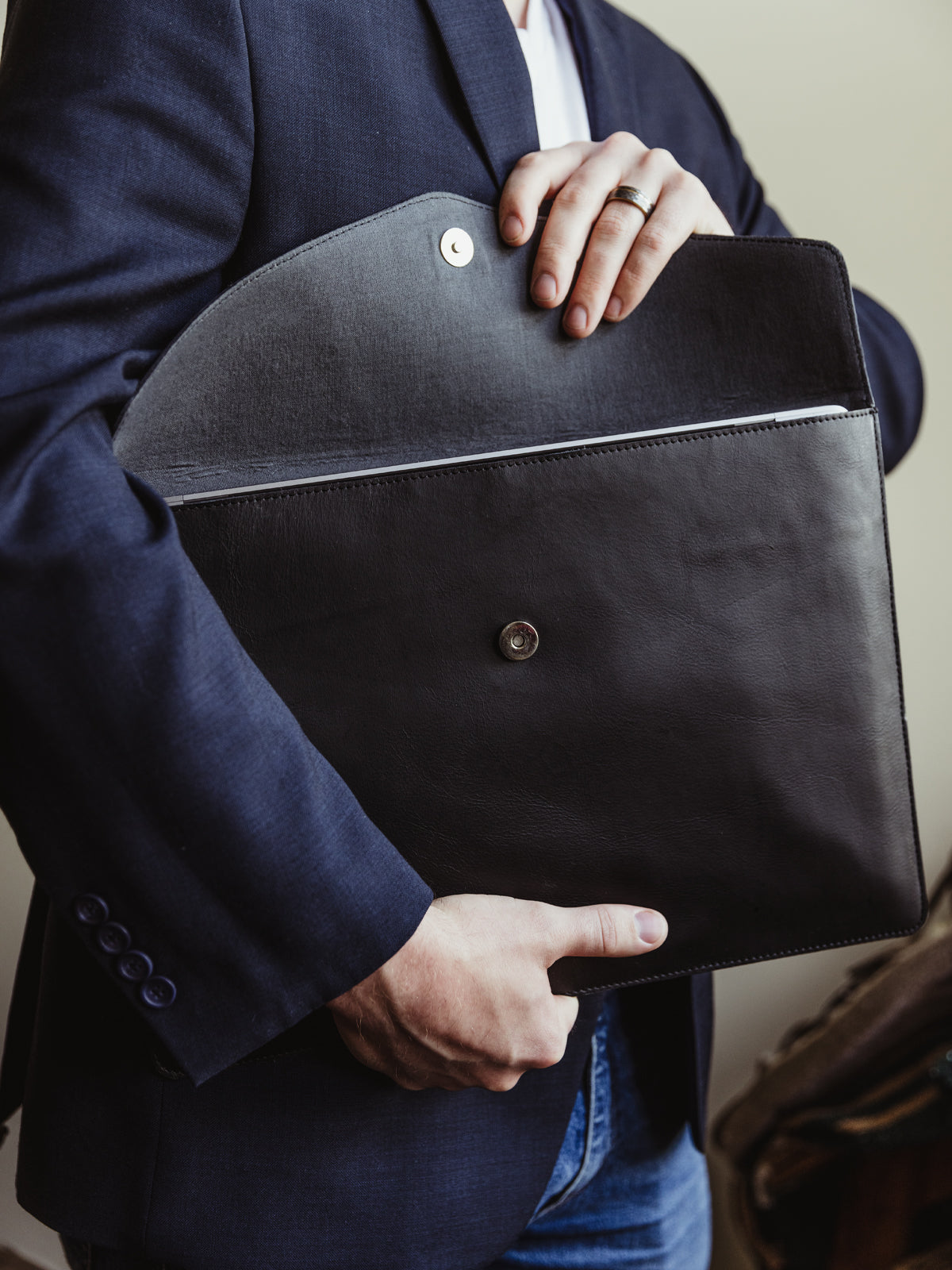 White male wearing a business blazer and jeans opening black envelope style laptop sleeve.