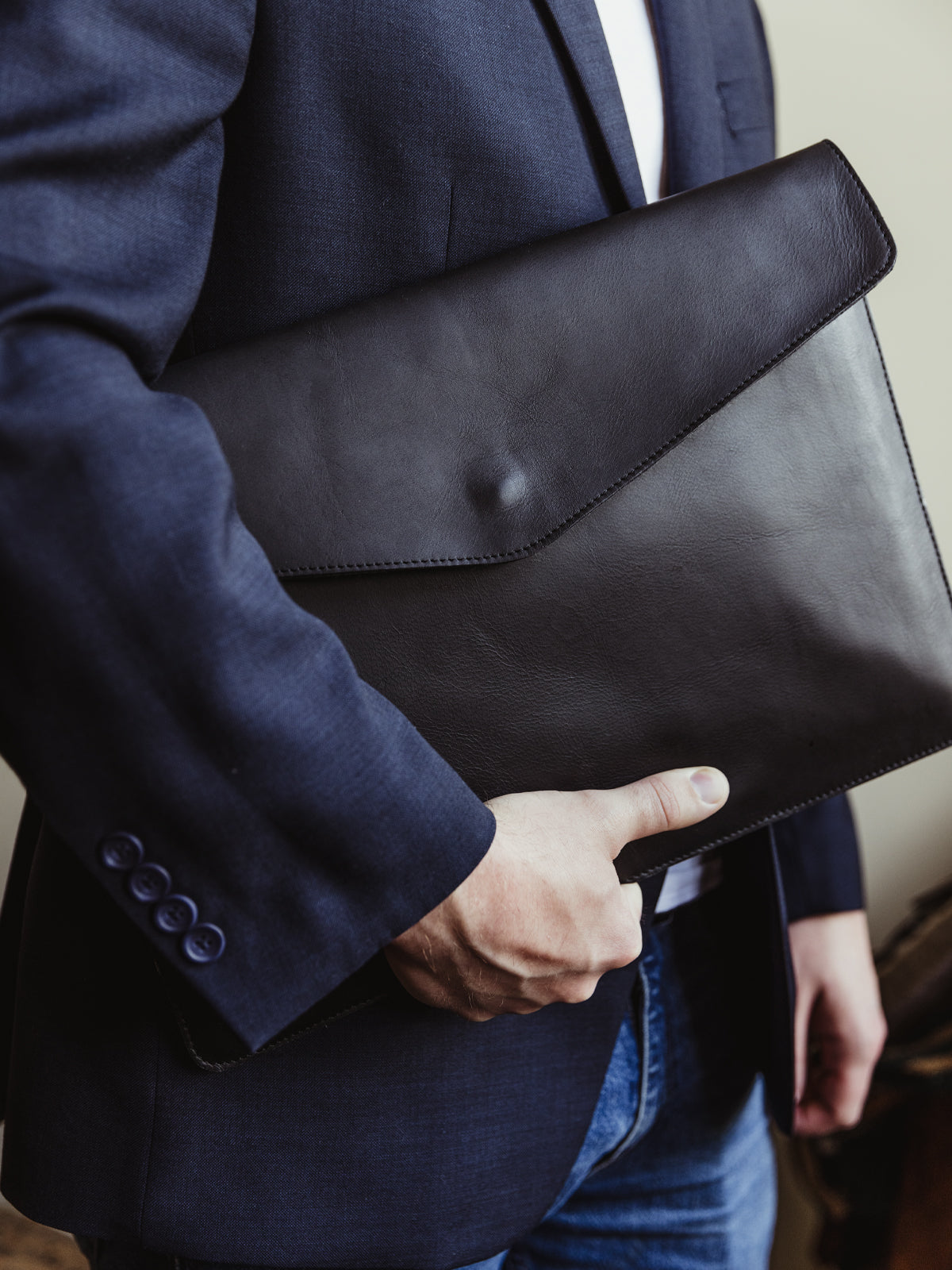 White male wearing a business blazer and jeans holding black envelope style laptop sleeve.