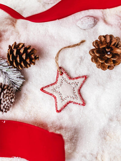 Handcrafted fabric star ornament with red stitching, placed on a snowy surface surrounded by pinecones and a festive red ribbon.