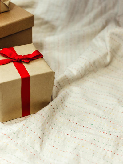 Holiday gift boxes wrapped in kraft paper with red ribbon, displayed on a soft, stitched fabric.