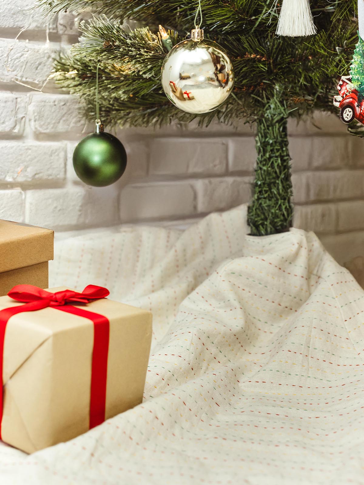 A beautifully wrapped gift box with a red ribbon, placed under a Christmas tree decorated with green and gold ornaments. 