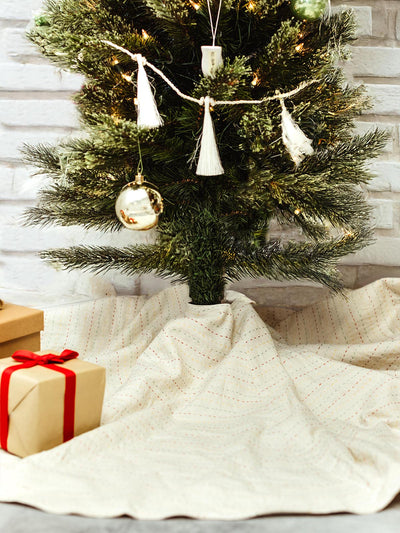 A Christmas tree adorned with white tassels and ornaments, surrounded by gift boxes wrapped in kraft paper with red ribbon. 