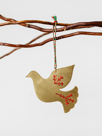 Handcrafted brass dove ornament featuring red embroidered branch details, hanging from a braided red and green string.