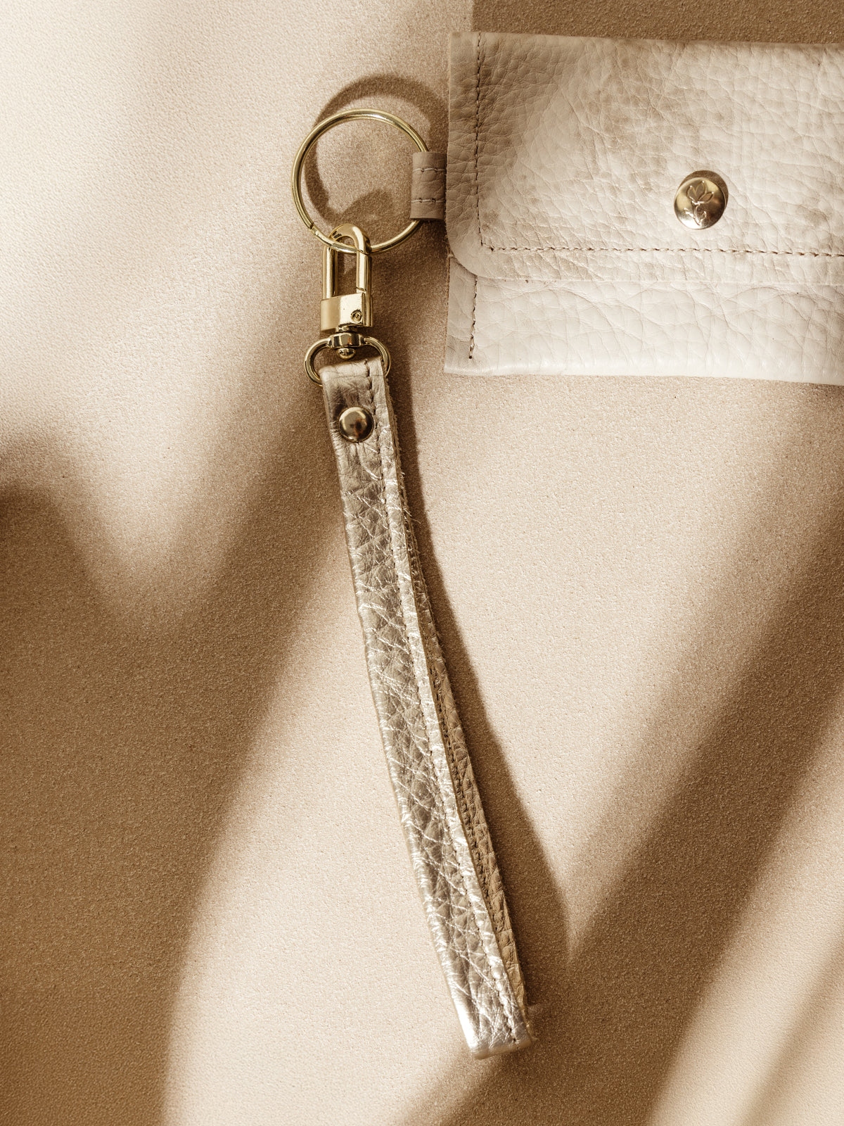 Close-up of a gold leather keychain with a sturdy clasp, attached to a beige leather pouch. A sleek and practical accessory for everyday organization.