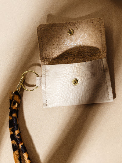 Beaudin beige leather coin pouch paired with a leopard print keychain, featuring gold hardware and a suede interior. A trendy and functional addition to everyday accessories.