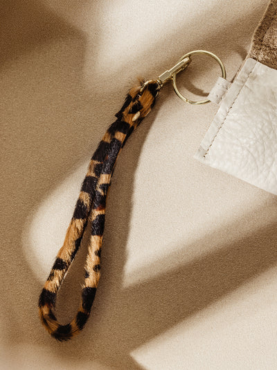 Stylish leopard print keychain attached to a beige leather coin pouch with gold hardware. A chic and functional accessory for everyday use.