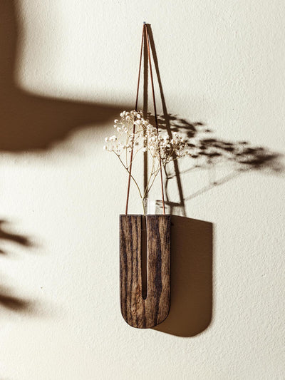 Handcrafted wooden wall vase in a U-shape, holding dried baby’s breath flowers, mounted on a cream-colored wall with soft shadows casting a natural effect.