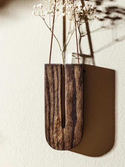 Close-up of a U-shaped wooden wall vase, displaying dried baby’s breath flowers in a minimalist design, hanging on a cream-colored wall with delicate shadows.