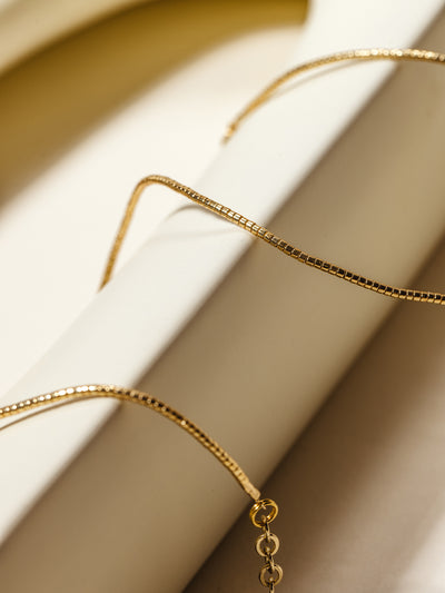 A close-up of a gold beaded necklace with an adjustable chain, styled over a sculptural ceramic object for a refined and modern aesthetic.