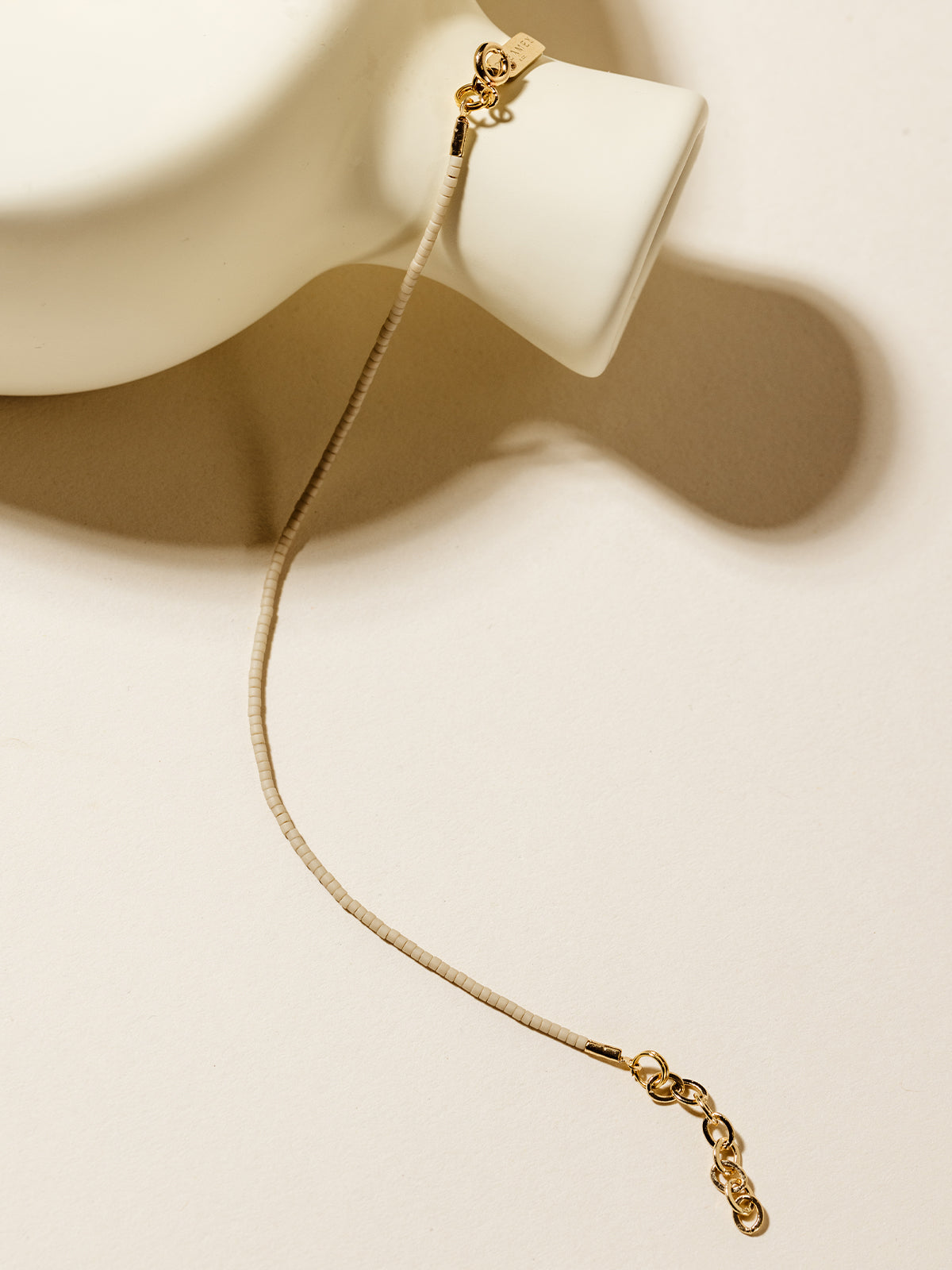 A neutral beige beaded bracelet with gold accents draped over a contemporary white ceramic vase, embodying simplicity and sophistication.