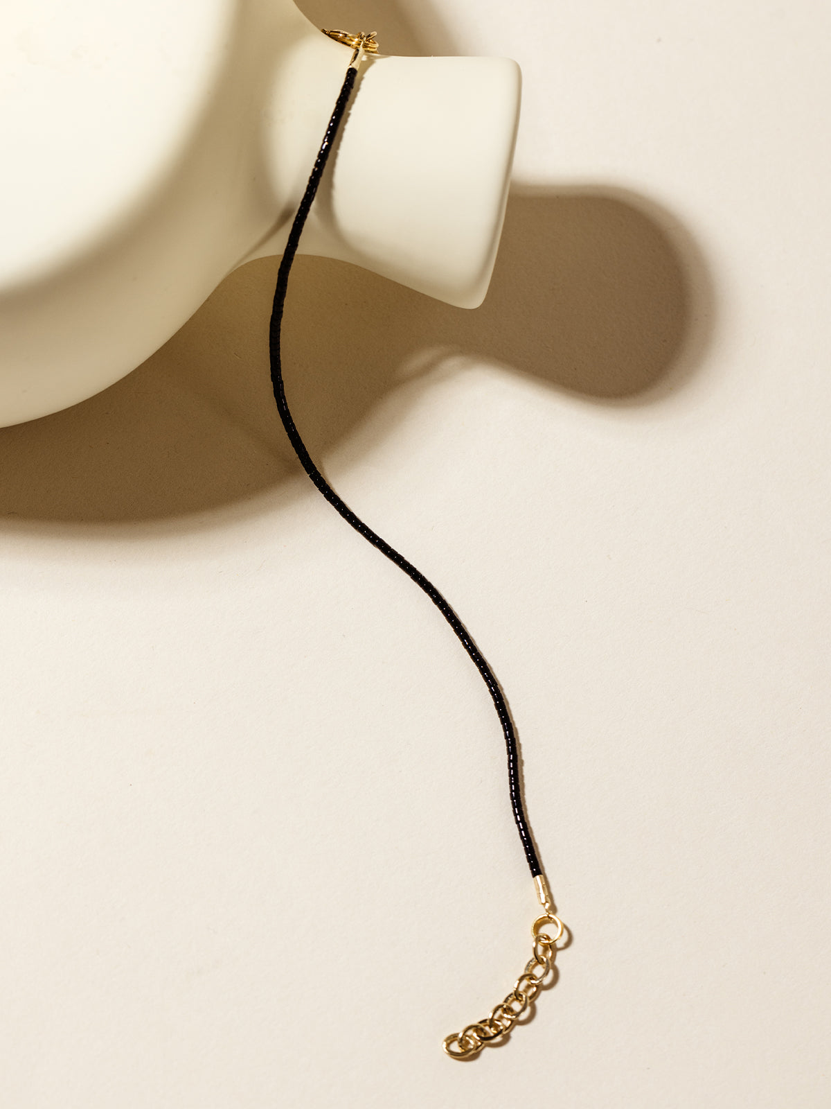 A black beaded bracelet with gold detailing elegantly arranged on a white ceramic vase, creating a contrast of bold and classic style.