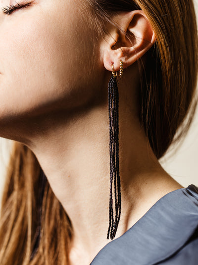 Close-up of a woman wearing black beaded tassel earrings with gold hoop accents, showcasing a chic and elegant accessory perfect for statement styling.