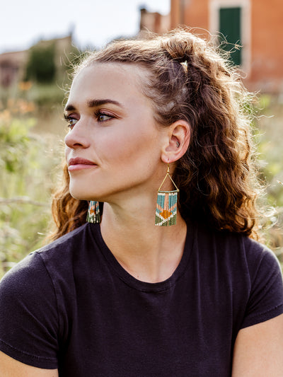 White  female model wearing fringe earrings with nature in the background. 