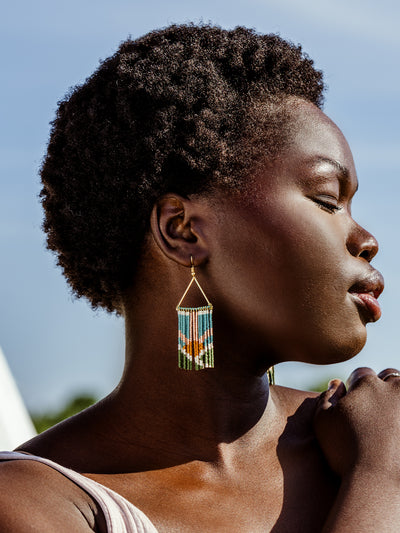 African female model wearing fringe earrings with blue sky in the background. 