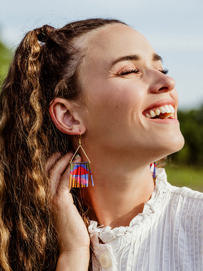 Female model laughing outside in nature wearing neon fringe earring with triangle top. 