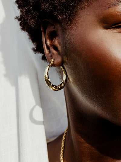 Closeup of female African model on white background wearing gold leaf of awareness hoop earrings.