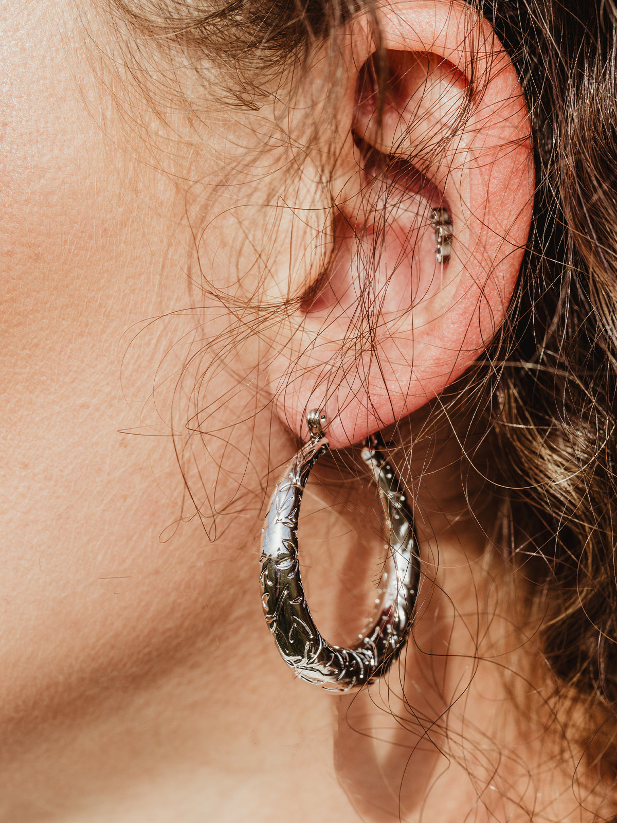 White female ear with silver leaf of awareness hoop earring. 